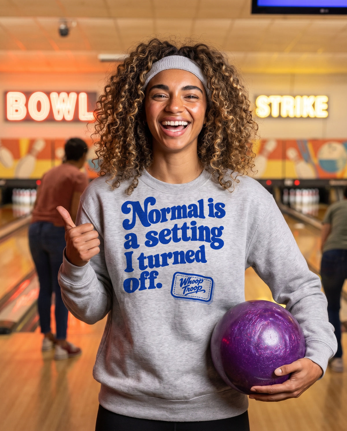 AI-generated image: a woman holding a bowling ball at a retro bowling alley, wearing the ash Normal is a Setting sweatshirt