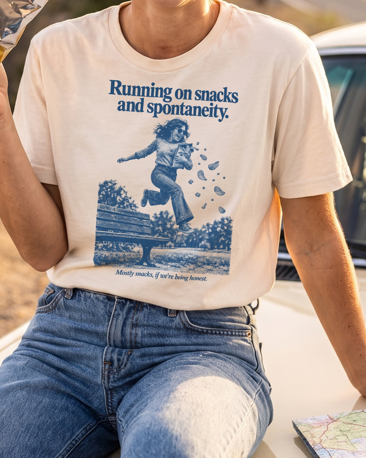 AI-generated image: close-up of the natural Running on Snacks tee, worn on a road trip with a bag of chips