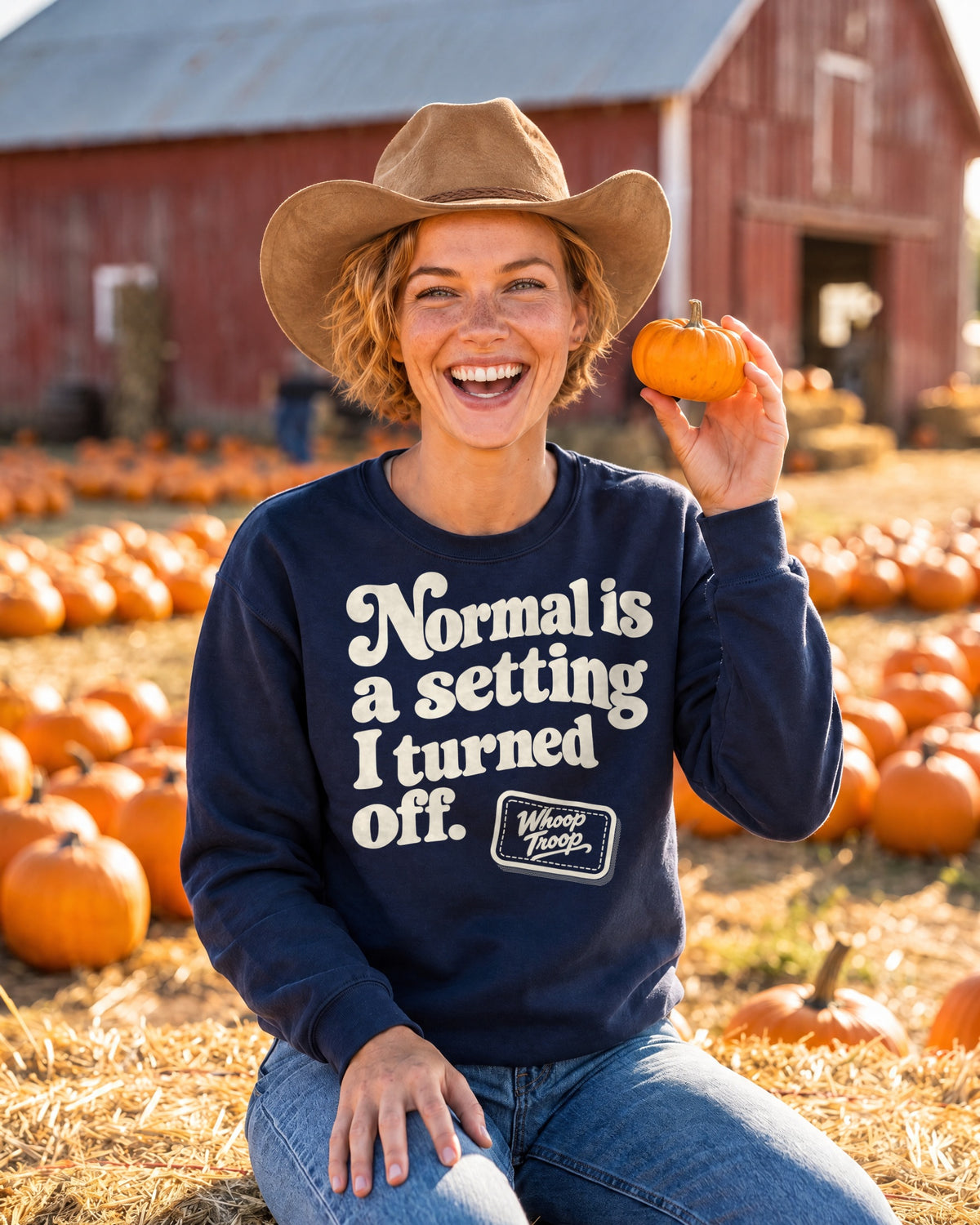 AI-generated image: a woman in a western hat on a hay bale at a pumpkin patch, wearing the navy Normal is a Setting sweatshirt